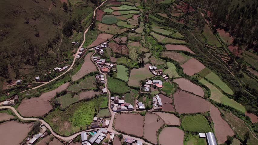Drone shot of a steep valley in the Andes with agricultural terraces and winding roads. Dramatic mountain landscape with patchwork fields.