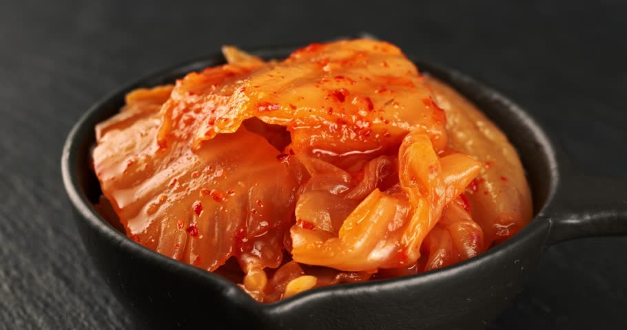 Bowl with korean traditional cabbage kimchi on dark background. Hot fermented napa cabbage. Close-up footage on the rotating table.