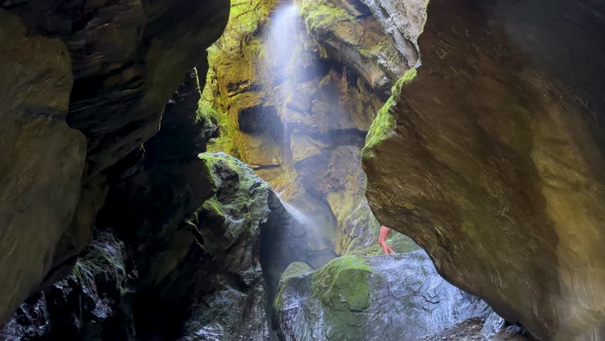 A girl walks out onto a rocky platform inside Wilsons Creek Chasm, Haast Pass, New Zealand. Towering cliffs and rushing water surround this dramatic and scenic gorge.