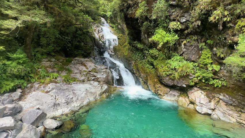 Christie Falls, a crystal-clear turquoise waterfall in Fiordland National Park, New Zealand. Towering cliffs, lush forest, and sparkling waters create a breathtaking alpine scene.