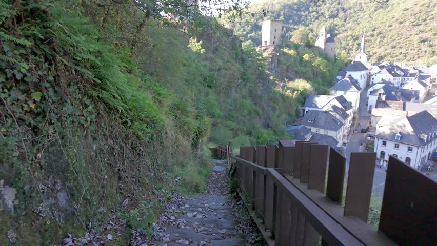 Esch-sur-Sure, Wiltz, Grand-Duche de Luxembourg, September 07, 2025, A tranquil pathway winds through lush greenery, offering stunning views of the picturesque town and bright skies
