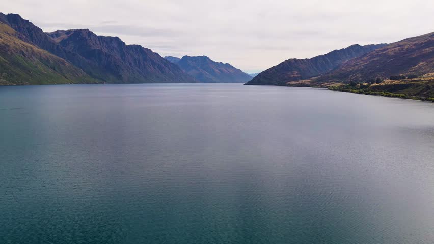 A 4K drone captures Kingston Lake in New Zealand, surrounded by rugged mountains. Calm waters and dramatic scenery highlight the natural beauty of this stunning landscape.