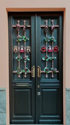 Wooden door with double panels decorated with Christmas wreaths on Italian facade. Symmetrical festive entrance decoration.
