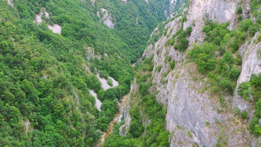 High-quality aerial footage showing a deep canyon with steep rocky cliffs and a river flowing at the bottom in Bosnia and Herzegovina. Dense green vegetation contrasts with exposed rock walls, creating a dramatic natural landscape suitable for documentaries, environmental storytelling, adventure travel, and nature-focused projects.