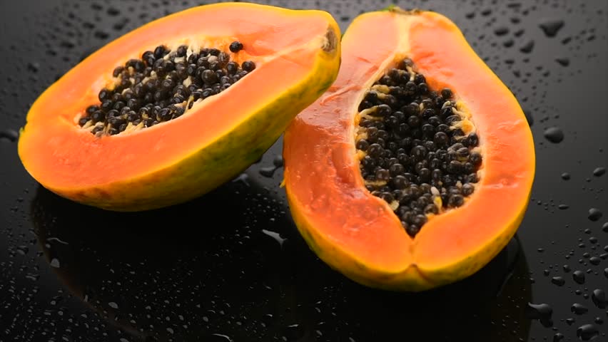 Papaya fruit on wet black background with water drops. Halved fresh organic Papaya exotic fruits close up. Slow motion, rotating 