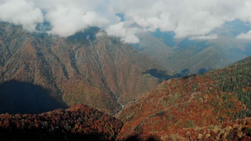 Mountain slopes covered with dense vegetation and autumn forest. Natural landscape of alpine valley with clouds.