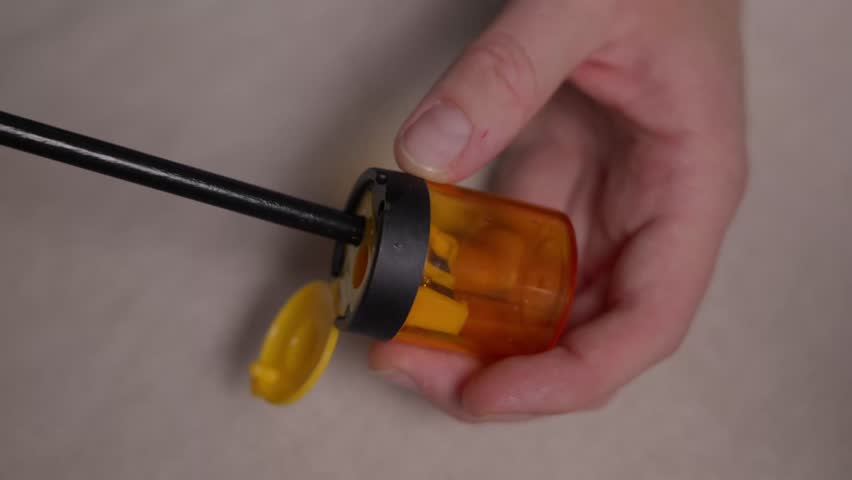 Close up of hands sharpening a pencil with a manual sharpener. Focus on rotation and wood shavings without face, showing a simple everyday stationery action. High quality 4k footage