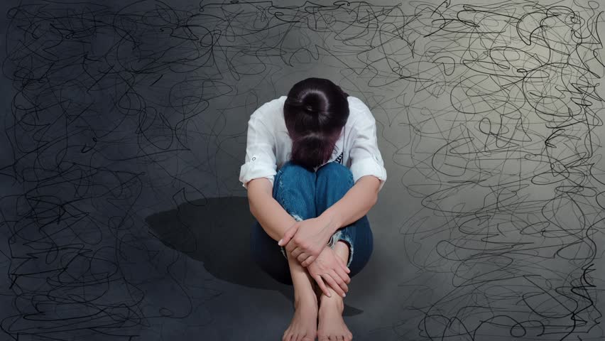 A woman sitting on the floor, hugging her knees, surrounded by words like Depression, Stress, and Anxiety, reflecting emotional struggles.