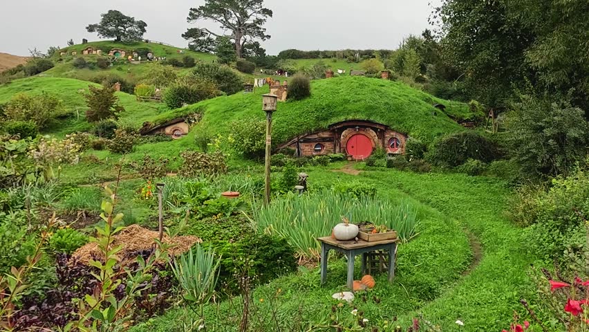 A view of a charming hobbit house surrounded by rolling green hills in Hobbiton, New Zealand. The iconic movie set showcases lush landscapes and magical countryside scenery.