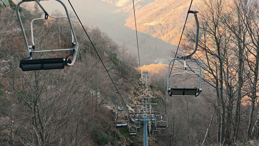 Inactive ski chairlift in off-season among bare trees with view of misty alpine peaks in autumn.