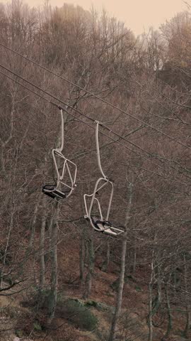 Inactive ski lift chairs hanging among bare forest in off-season on alpine slope.