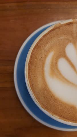Blue cup of latte with a donut on a plate, placed on a wooden café table. Warm and cozy coffee shop atmosphere perfect for lifestyle, food, and café-themed