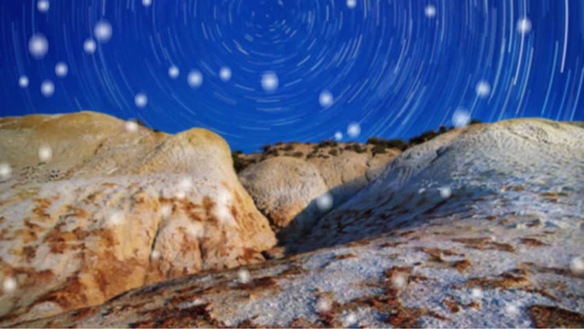 "A vibrant long-exposure shot of circular star trails in a deep blue night sky rotating over a rugged, rocky desert landscape with soft bokeh light effects."
