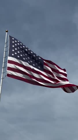 An American flag with stars and stripes proudly waving in the wind against a blue sky, a symbol of freedom for the United States	
