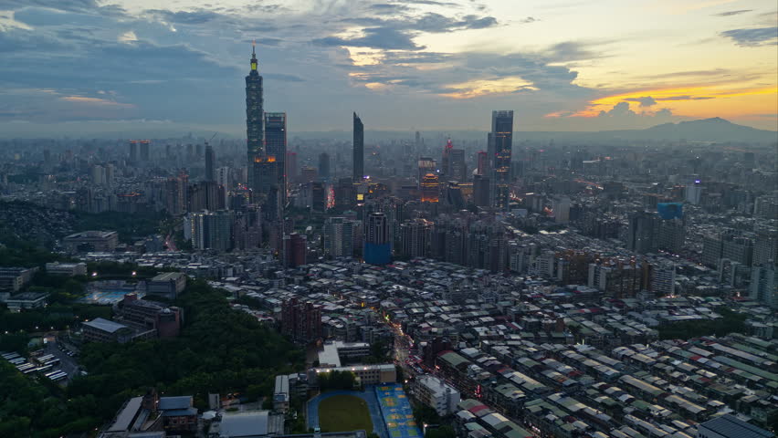 Aerial hyperlapse footage in a rotational motion above Downtown Taipei at dusk, the vibrant capital city of Taiwan, with 101 Tower standing out amid modern skyscrapers in XinYi Commercial District, city lights dazzling under twilight sky and Guanyin Mountain dominating the distant horizon.

This footage is an aerial hyperlapse of the vibrant city of Taipei at night, focusing on the iconic Taipei 101 skyscraper. The visual effect, achieved with a drone, makes the city lights and traffic appear to move in fast forward while the viewpoint smoothly rotates or tracks around the tower, showcasing the bustling Xinyi Commercial District and surrounding cityscape against a backdrop of mountains (Guanyin and Datun Mountains) on the horizon under the evening sky.