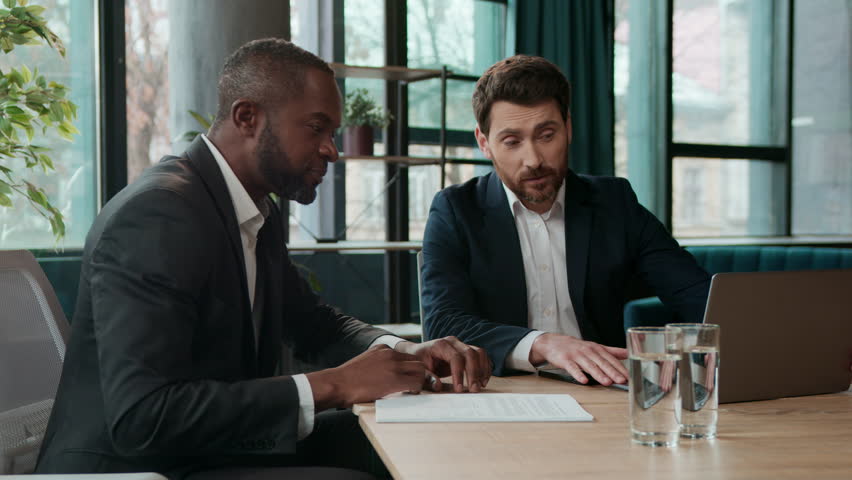 Multiracial business men office team businessmen guys talking writing notes in documents signing papers African American Caucasian colleagues working teamwork financial agents discuss laptop startup