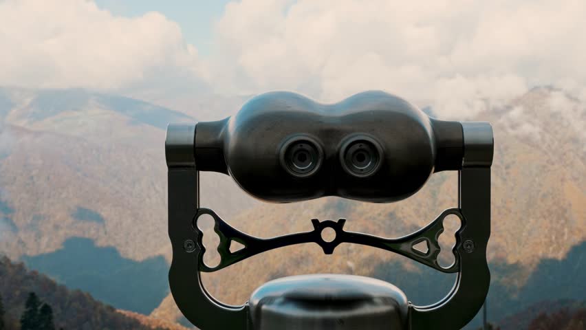 Tourist binoculars at viewpoint with dramatic view of misty alpine peaks and clouds.