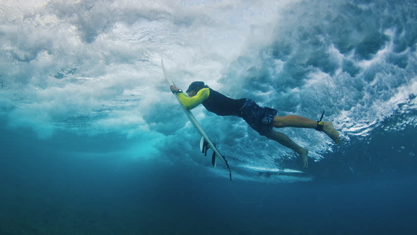 Surfer under the wave. Underwater view of the adult male surfer diving under the wave with surf board