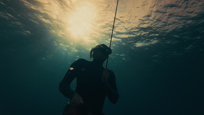 Freediver trains on the buoy and rope in the open sea at sunset