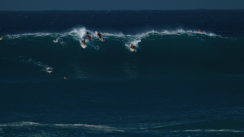 Big wave surfing in Hawaii on Waimea Bay. People surf the huge ocean wave breaking on the Hawaiian shore in Waimea Bay. Surfers share the wave in Hawaii. Oahu island
