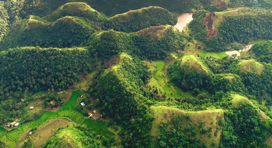 Aerial panoramic view of lush green tropical hills and a serene lake.