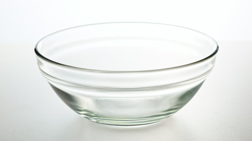 Honey pours into a transparent bowl on white background. Wooden honey spoon dips into honey, lifts slowly and thick drop flows down. Close up shot showing texture, viscosity and natural sweetness.