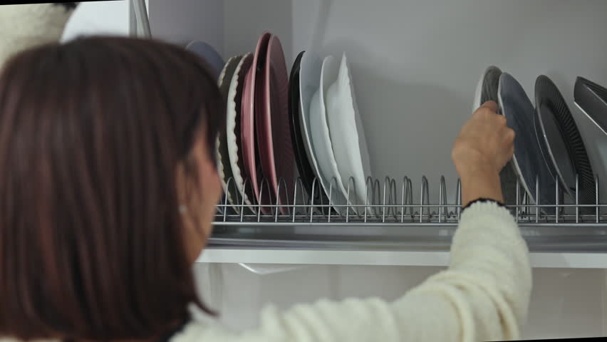 Woman cleans kitchen at home, wipes cabinets and shelves,places plates, rinses cloth, moves muffins into container.Pregnant female rests,drinks water,wipes kitchen counter and puts spoons into drawer.