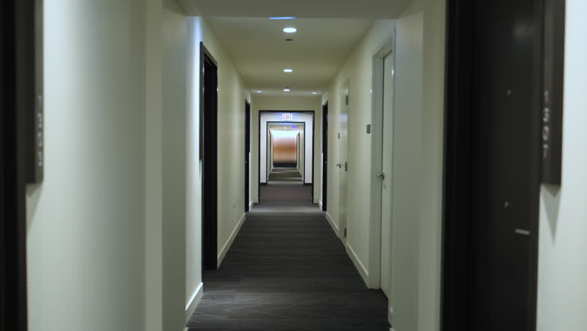 Long symmetrical hotel hallway with repeating doors and soft lighting, creating a clean, modern, and slightly cinematic interior perspective. POV view