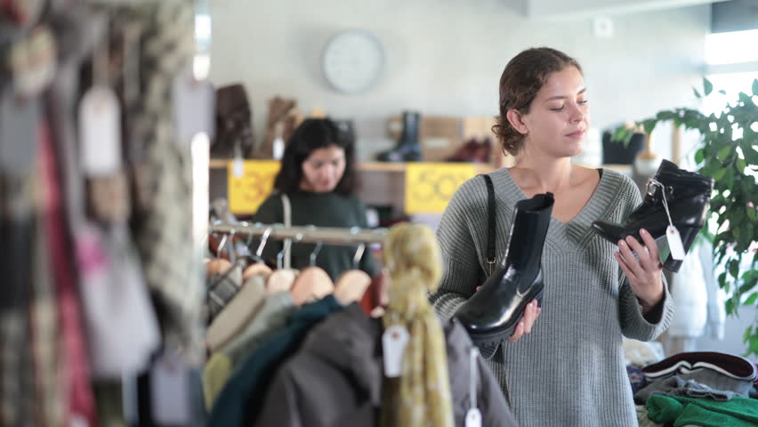 European woman stands in a shoe store and chooses heeled ankle boots and platform boots. Woman buying shoes on sale in a store. High quality 4k footage