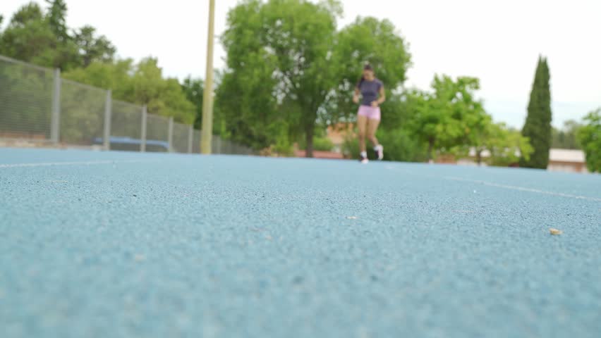 Low angle view of a woman athlete jogging towards the camera on a blue running track in a stadium