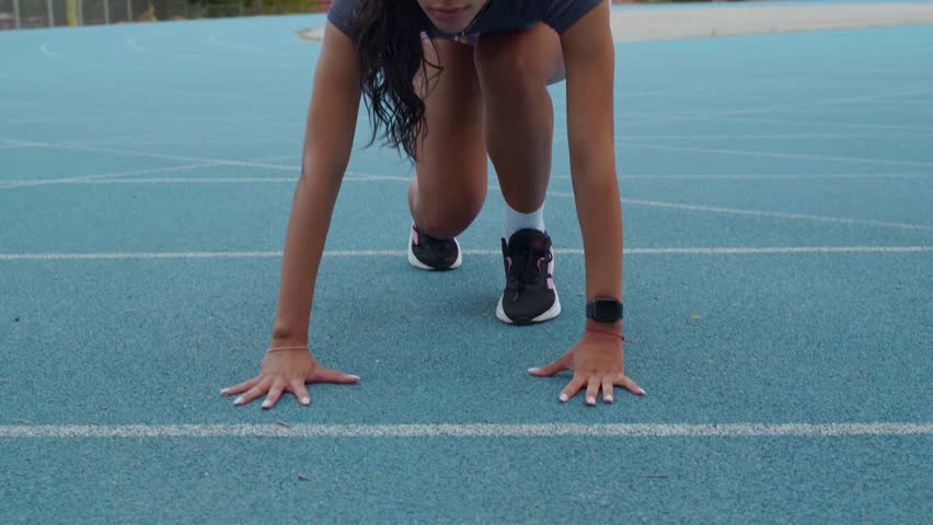 Focused young sportswoman in a starting block position on a track, ready for a sprint competition