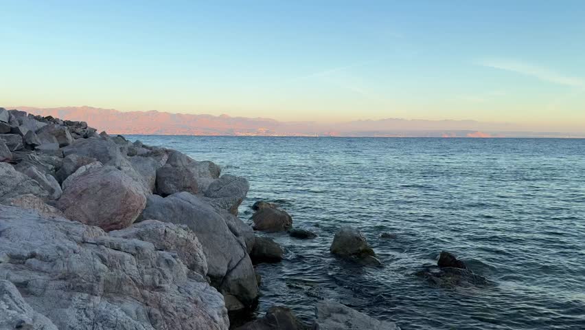 Rocky shoreline along the Gulf of Aqaba in South Sinai, Egypt. Calm blue seawater meets coastal rocks under a clear sky, showcasing the natural beauty of the Red Sea region.