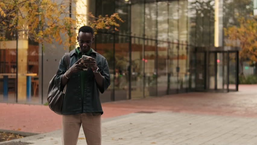 A young man smiles while looking at his phone. He