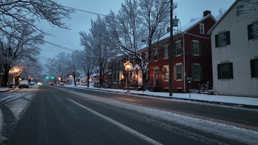 Low angle shot of icy and muddy street after snowfall in American town. Decorated streets and shops along downtown road of Lititz, PA. Leafless trees frozen with ice on cloudy dawn.