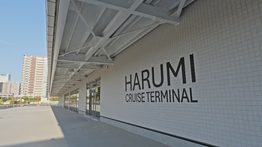 Modern exterior of the re-opened Harumi Cruise Terminal in Tokyo, Japan, featuring a clean white wall and sign.