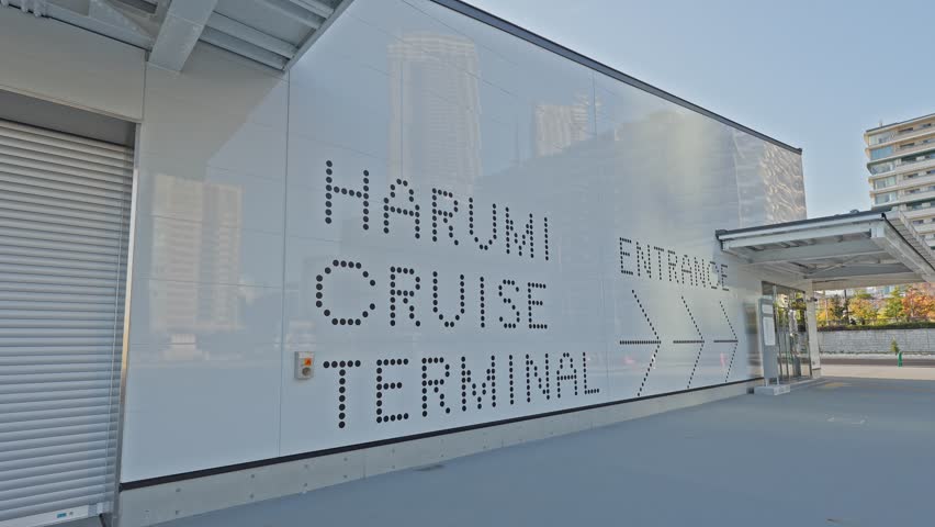 A focused, professional shot of the "HARUMI CRUISE TERMINAL" and "ENTRANCE" directional signage displayed on the modern, white facade of the passenger terminal building in Tokyo.