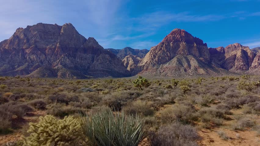 Smooth afternoon aerial view of a red rock canyon, showcasing sunlit rock formations and arid desert landscape.