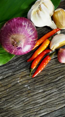 Top down view of red onion garlic cloves and red chili peppers with green leaf on dark textured wooden surface