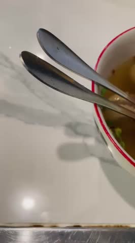 Close-up footage of Indonesian bakso soup with meatballs, tofu, crispy fried wonton, and clear savory broth, served in a bowl with fresh herbs.
