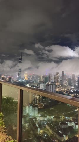 Night view of Kuala Lumpur city skyline with glowing lights and clouds drifting across the urban landscape, creating a cinematic and atmospheric city scene.