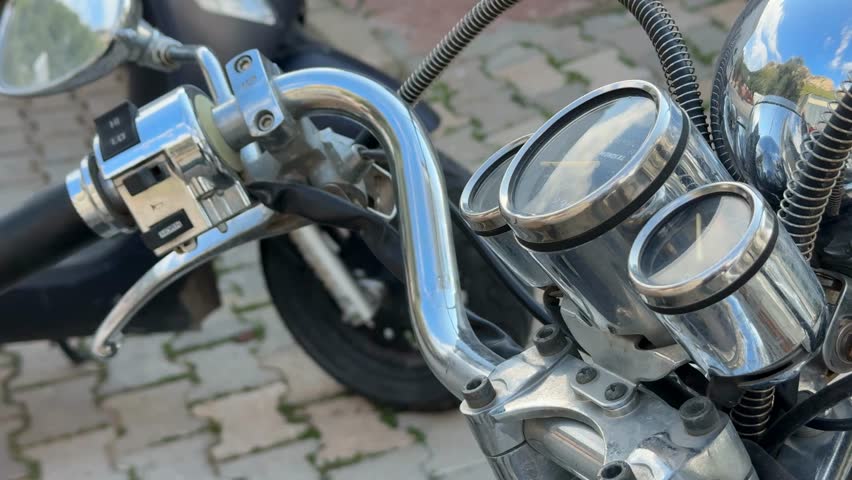 Motorcycle handlebar and gauges with chrome details, parked on stone pavement background video