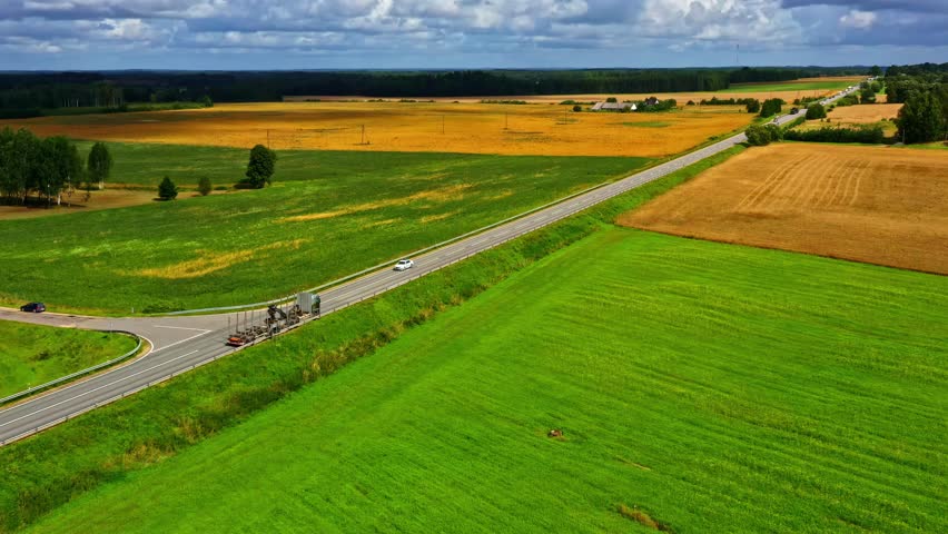 Military convoy driving through countryside road between green farm fields