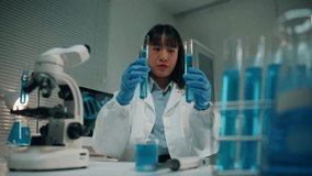 Young Asian female researcher in a white lab coat and gloves comparing two test tubes with blue chemical liquid in a modern laboratory - Powered by Shutterstock - Get 15% off with code: PIKWIZARD15