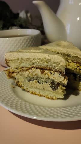 A piece of cake with cream in a plate on a pink table, a mug of tea and a kettle in the background. Tea party, snack. Sweet Cert