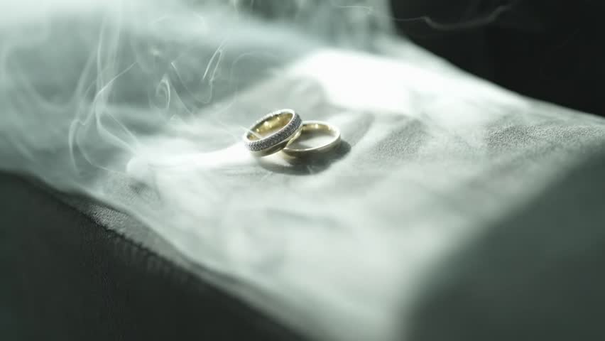 Luxury wedding rings resting on a soft white surface, enveloped in a romantic ethereal mist that creates a dreamlike and sophisticated atmosphere for a ceremony, Slow motion orbit.