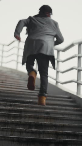 Young black man running up over outdoors stairs, back view, slow motion. Walk in city in autumn day, hurrying passerby, be late on important meeting, rising up over staircase, make successful career