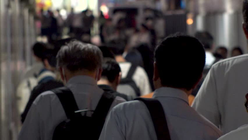 TOKYO, JAPAN - AUG 2025 : Crowd of people walking at the street near the station in busy night rush hour. Japanese people, urban city life and lifestyle concept video. Slow motion shot.