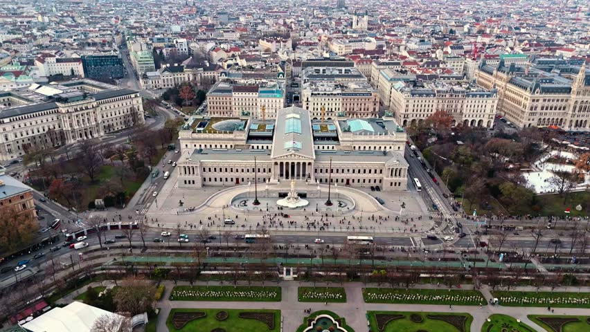 Aerial drone shot panning right of the Austrian Parliament Building, revealing the Vienna cityscape with historic architecture, wide avenues, and surrounding rooftops illuminated by low winter sun.