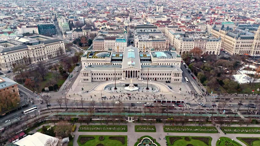 Static aerial drone shot of the Austrian Parliament Building in Vienna, framed by the surrounding cityscape with historic rooftops and broad avenues, illuminated by clear winter sunlight