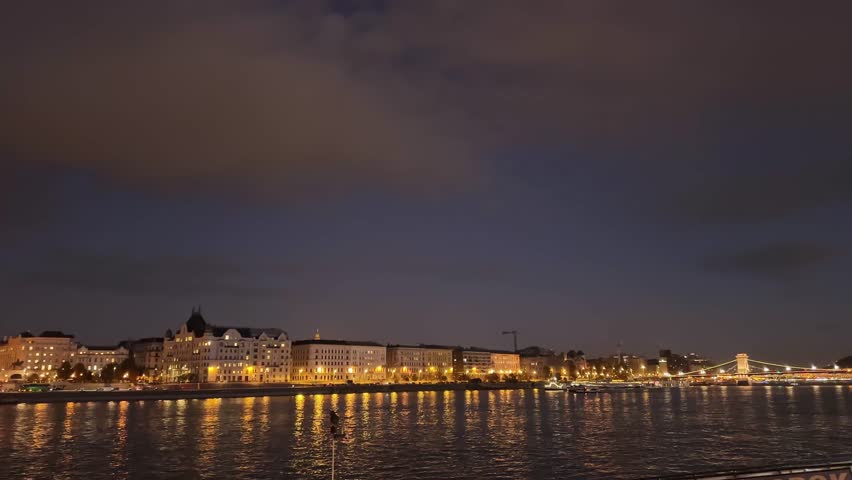 East Danube river bank with Hungarian Parliament Building with night illumination, view from the opposite bank while panning at evening
